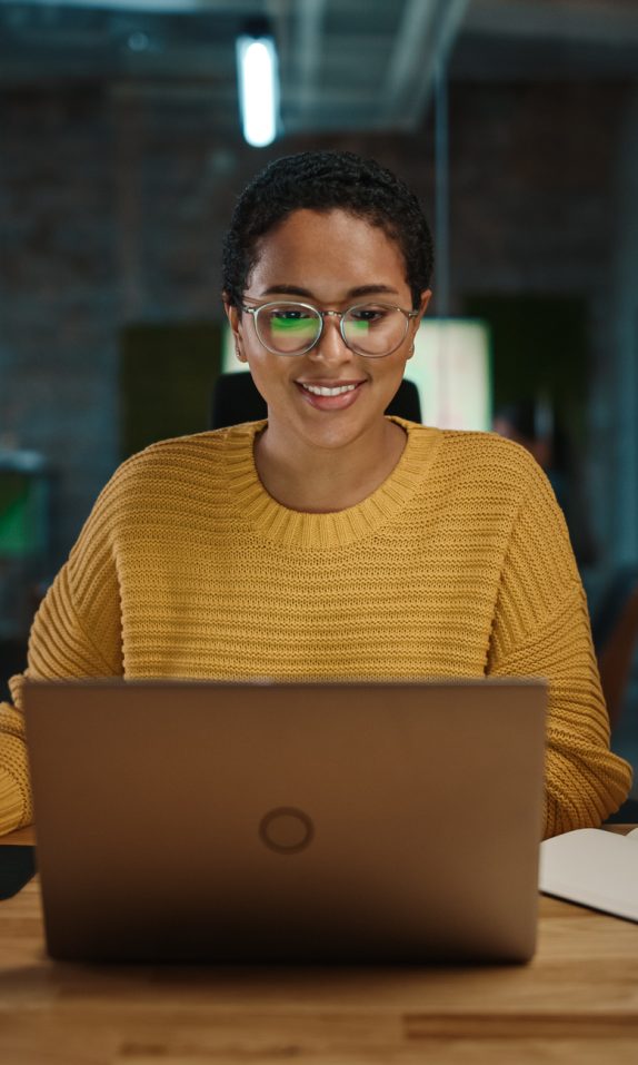 Portrait of Young Latina Marketing Specialist Working on Laptop Computer in Busy Creative Office Environment. Beautiful Diverse Multiethnic Female Project Manager is Browsing Internet.